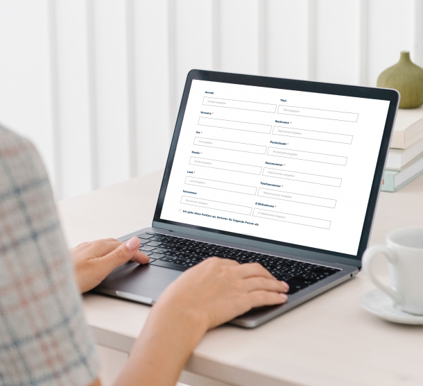 Ein Mensch, das Gesicht ist nicht erkennbar, sitzt an einem Tisch und gibt an einem Laptop Daten in ein Formular ein.