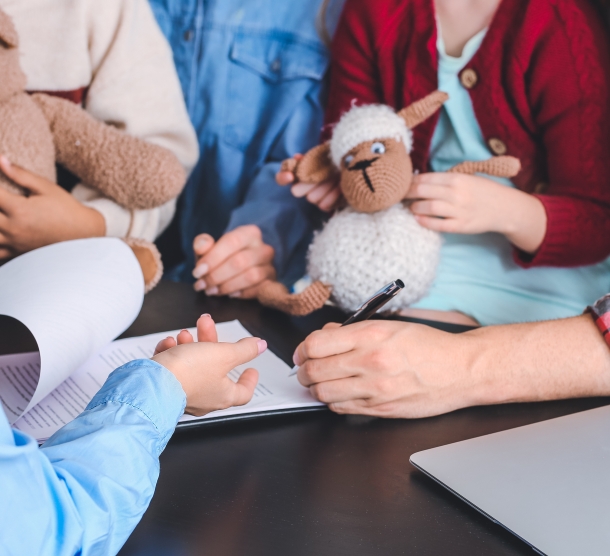 Erwachsene und Kinder, deren Gesichter nicht zu sehen sind, sitzen an einem Tisch und besprechen sich über ein Dokument gebeugt.