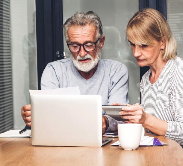 Ein Mann und eine Frau sitzen mit zwei Kaffeetassen an einem Tisch vor einem Laptop.